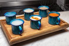 six blue mugs on a wooden tray filled with liquid