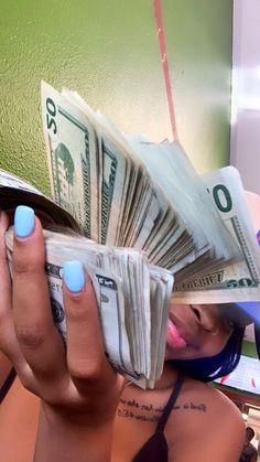 a woman with blue nail polish holding money in front of her face and looking at the camera