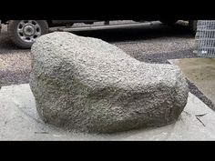 a large rock sitting on top of a cement slab next to a parked car in a parking lot