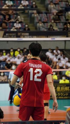 two men in red uniforms playing volleyball on a court with people watching from the stands