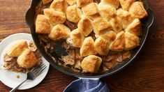 a casserole dish filled with meat and bread on a wooden table next to a fork