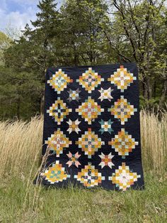 a black quilt with yellow and green stars on it in the grass near some trees