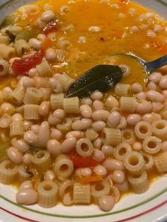 a white bowl filled with pasta and vegetables next to a spoon on top of a table