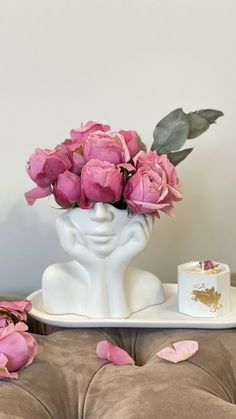 a white vase filled with pink flowers on top of a table next to a cup