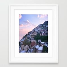 a framed photograph of the city of positi, italy at sunset with clouds in the sky