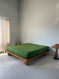 a green bed sitting in the middle of a room next to a lamp and window