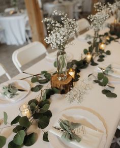 the table is set with white plates and silverware, greenery and candles are on the tables