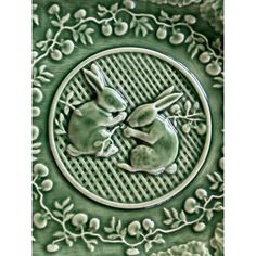 two rabbits are sitting in the center of a green plate with vines and leaves on it