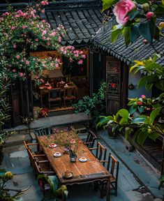 an outdoor dining area with wooden table and chairs, surrounded by greenery and flowers