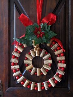 a wreath made out of wine corks hanging on a wooden door with red ribbon