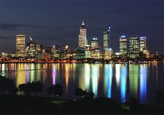 the city is lit up at night and reflecting in the water