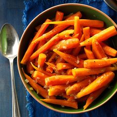 a bowl filled with sliced carrots next to a spoon and fork on a blue cloth