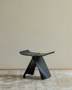 a black stool sitting on top of a carpeted floor next to a white wall