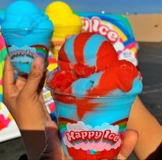 someone holding up two ice creams in their hands, one is blue and the other is red