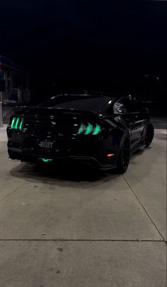 a black sports car with green lights on it's hood parked in a parking lot