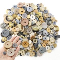 a hand is holding a bunch of buttons in front of a pile of other buttons