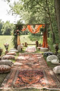 an outdoor area with lots of pillows and rugs on the ground, surrounded by trees