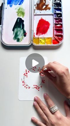 a woman is painting with her hands on the paper next to some watercolors