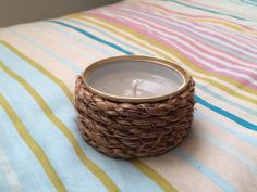 a wicker candle holder sitting on top of a striped bed sheet with a gold rim