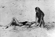 two women are laying on the beach in their bathing suits