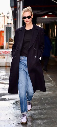 a woman in black coat and jeans walking down the street