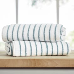 two white and blue striped towels sitting on top of a wooden table next to a window