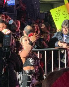 a woman is standing in front of a crowd and taking pictures with her cell phone