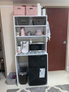 a microwave oven sitting on top of a white shelf next to a black refrigerator freezer