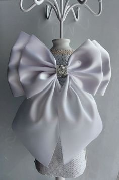 a white dress with a large bow on it's back hanging from a coat rack