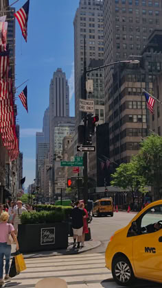 a yellow taxi cab driving down a street next to tall buildings with american flags flying in the air