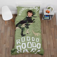 a little boy laying in bed with a green dinosaur duvet cover and pillowcase