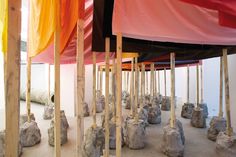 an art exhibit with rocks and poles in the center, surrounded by colorful fabric draped over them