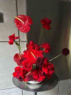 red flowers are in a white vase on a small table next to a metal wall