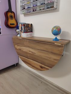 a wooden shelf with a guitar on it in front of a purple wall and bookshelf