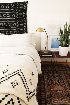 a bed with white sheets and pillows in a room next to a potted plant