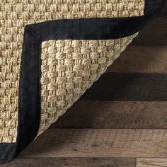 a close up view of a black and tan area rug on wooden flooring with wood planks in the background