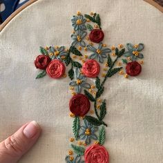 a hand is stitching a cross with flowers on it