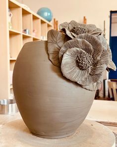 a clay vase with two flowers on it sitting on a table in front of bookshelves