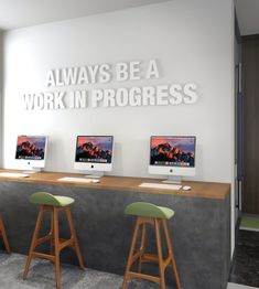 three computer monitors sitting on top of a counter in front of a wall that says, always be a work in progress