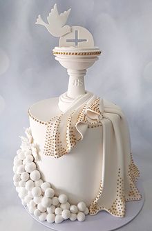 a white cake with a cross on top and pearls around the edges, sitting on a table