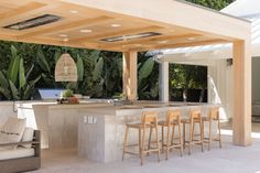 an outdoor kitchen with bar stools next to it and lots of greenery in the background