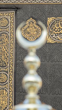 an intricately decorated wall with arabic writing on it and a metal object in the foreground