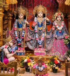 three statues of hindu deities in front of a stage with flowers on the floor and other decorations