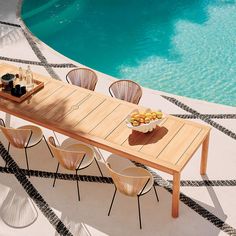 a wooden table sitting next to a swimming pool with chairs and plates of food on it