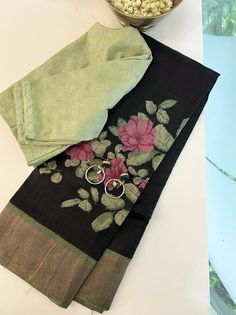 Black handloom Tussar saree adorned with pista green buttercup floral handprints and a matching zari border. The zari-striped pista green blouse and palla with thick zari bands complete the ensemble. Paired effortlessly with a pista green pure silk blouse and statement green silver earring. Simple Blouses, Beaded Wedding Jewelry, Long Blouse Designs, Sarees For Girls, Latest Blouse Designs Pattern, Cotton Saree Blouse Designs, Silk Sarees With Price, Floral Print Sarees, Latest Model Blouse Designs