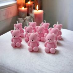 small pink teddy bears sitting on top of a bed next to two candles and a window