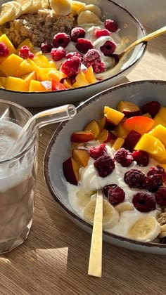 two bowls filled with fruit and yogurt on top of a wooden table next to a glass of milk