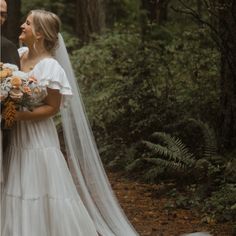 a bride and groom standing in the woods with their wedding veil blowing over her face