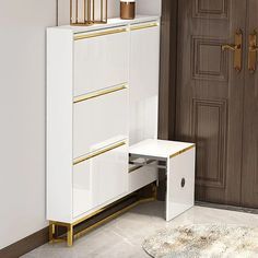 a white cabinet with gold handles and drawers in front of a brown door, next to a rug on the floor