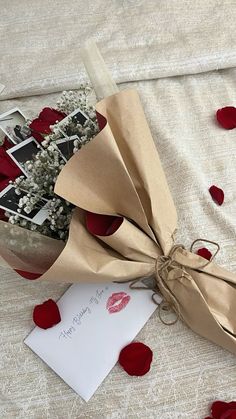 a bouquet of roses and a card tied to it on a bed with petals scattered around